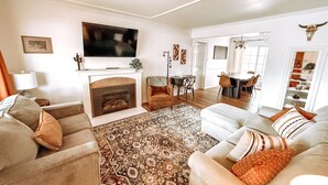 A living room with a fireplace, a television, a dining area, and a kitchen visible through an open door. - Centrally Located, Family friendly Home- With Game Room and Infrared Sauna (Farmington)