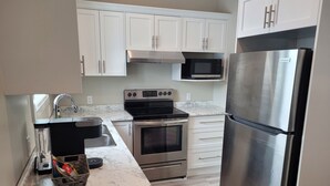 A modern kitchen with white cabinets, stainless steel appliances, a marble countertop, and a built-in oven. - Small Town Charm (Clifford)