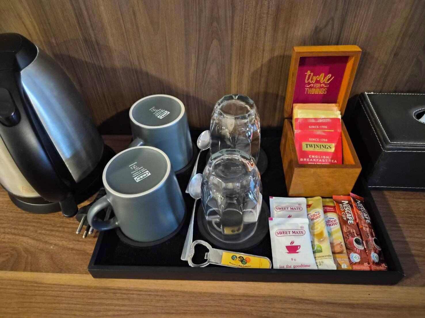 A tray with a coffee maker, two mugs, a glass carafe, a box of Twinings English Breakfast Tea, and packets of Sweet Mate tea.