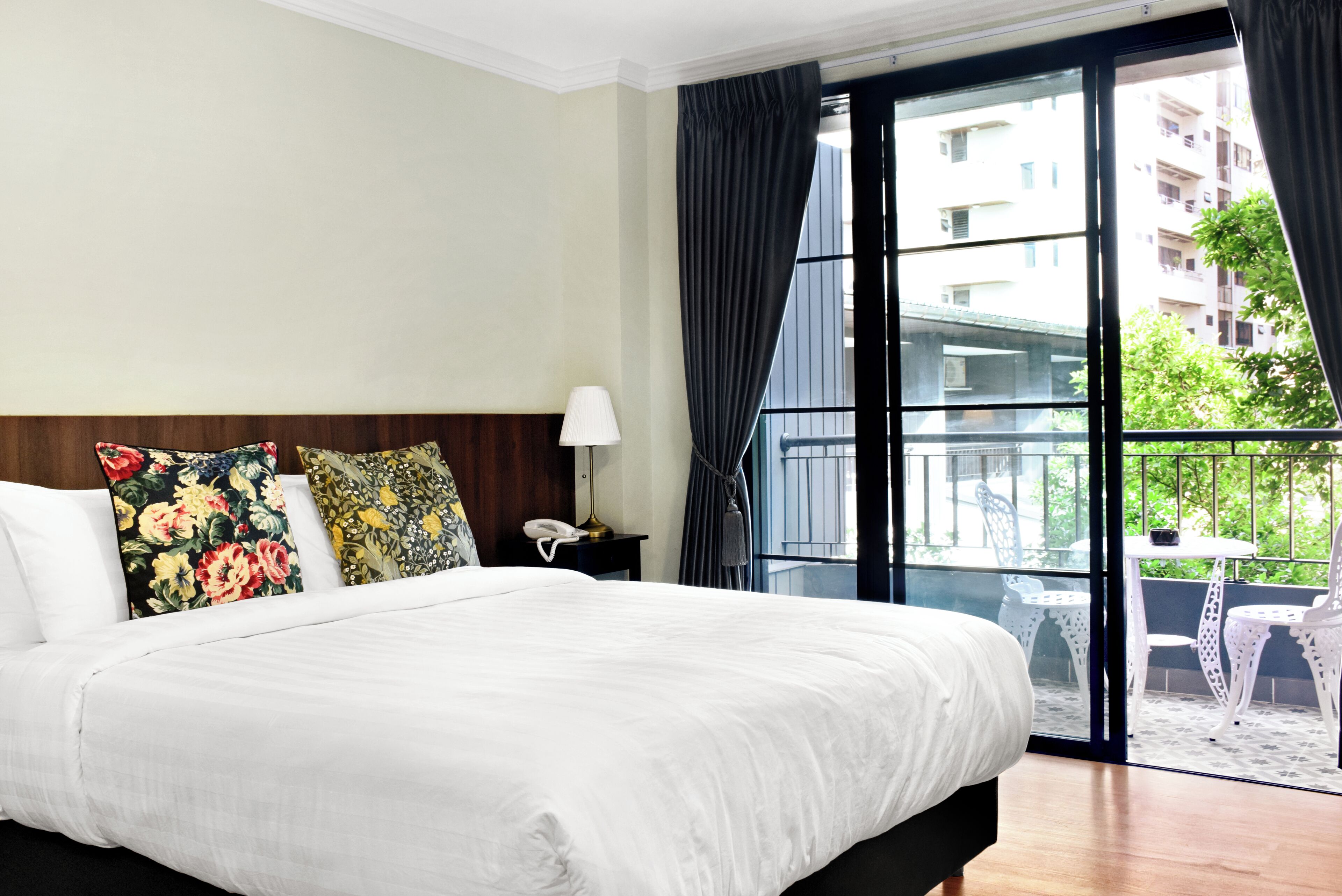 A hotel room with a large bed, a nightstand with a lamp, and a view of the outside balcony.