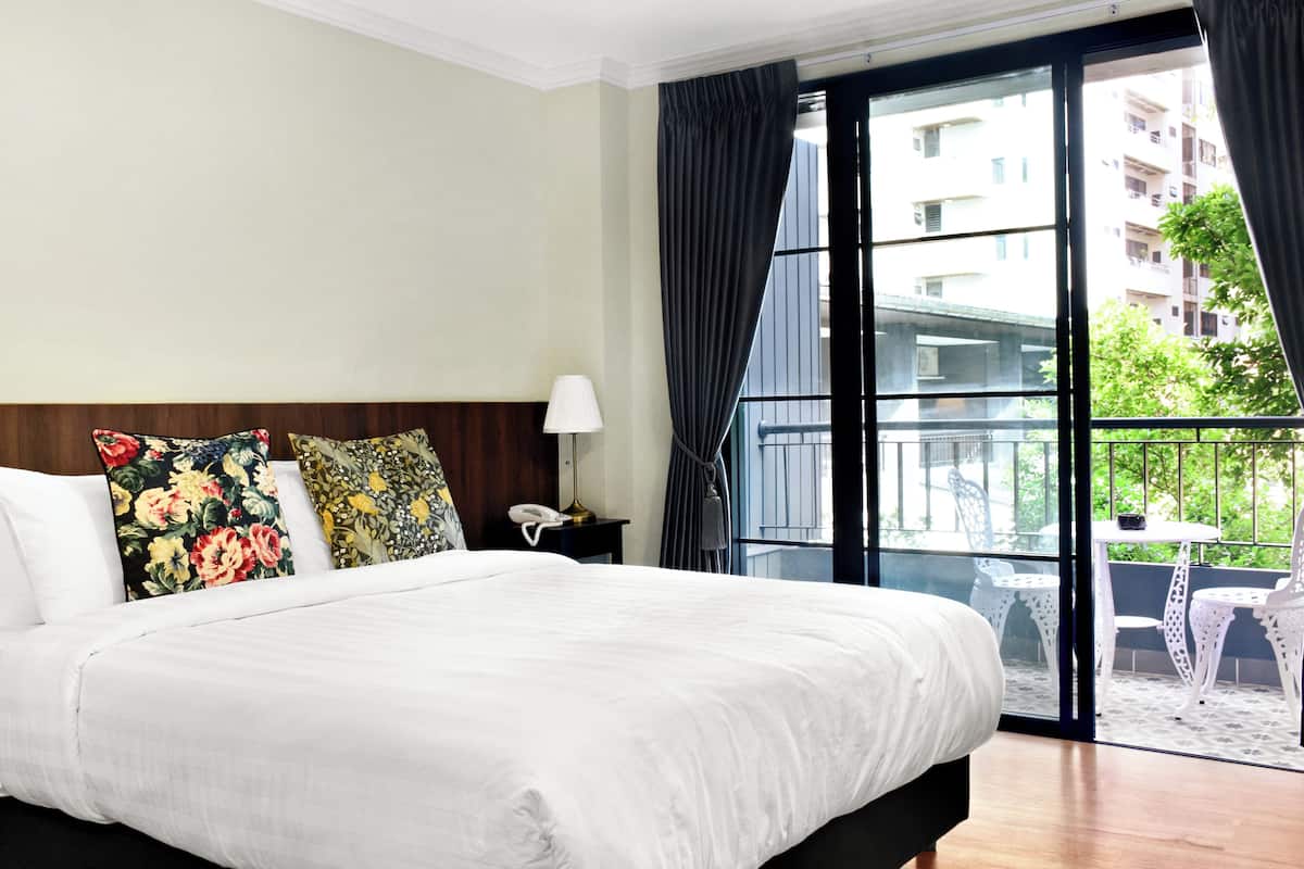 A hotel room with a large bed, a nightstand with a lamp, and a view of the outside balcony.