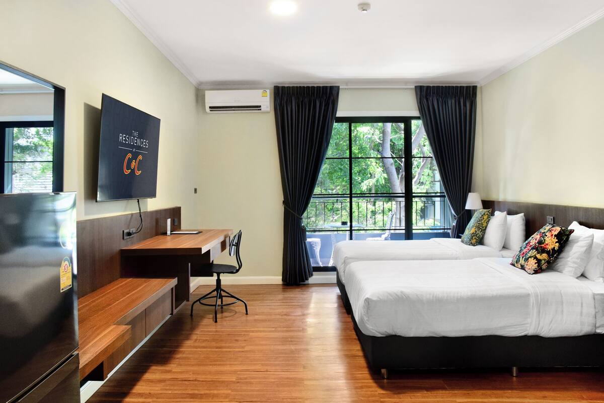 A hotel room with a bed, desk, chair, TV, and large windows.