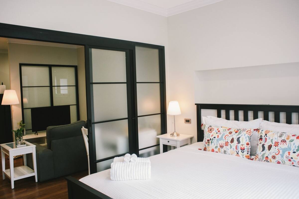 A hotel room with a bed, a chair, a nightstand, a lamp, and a large window with frosted glass panels.