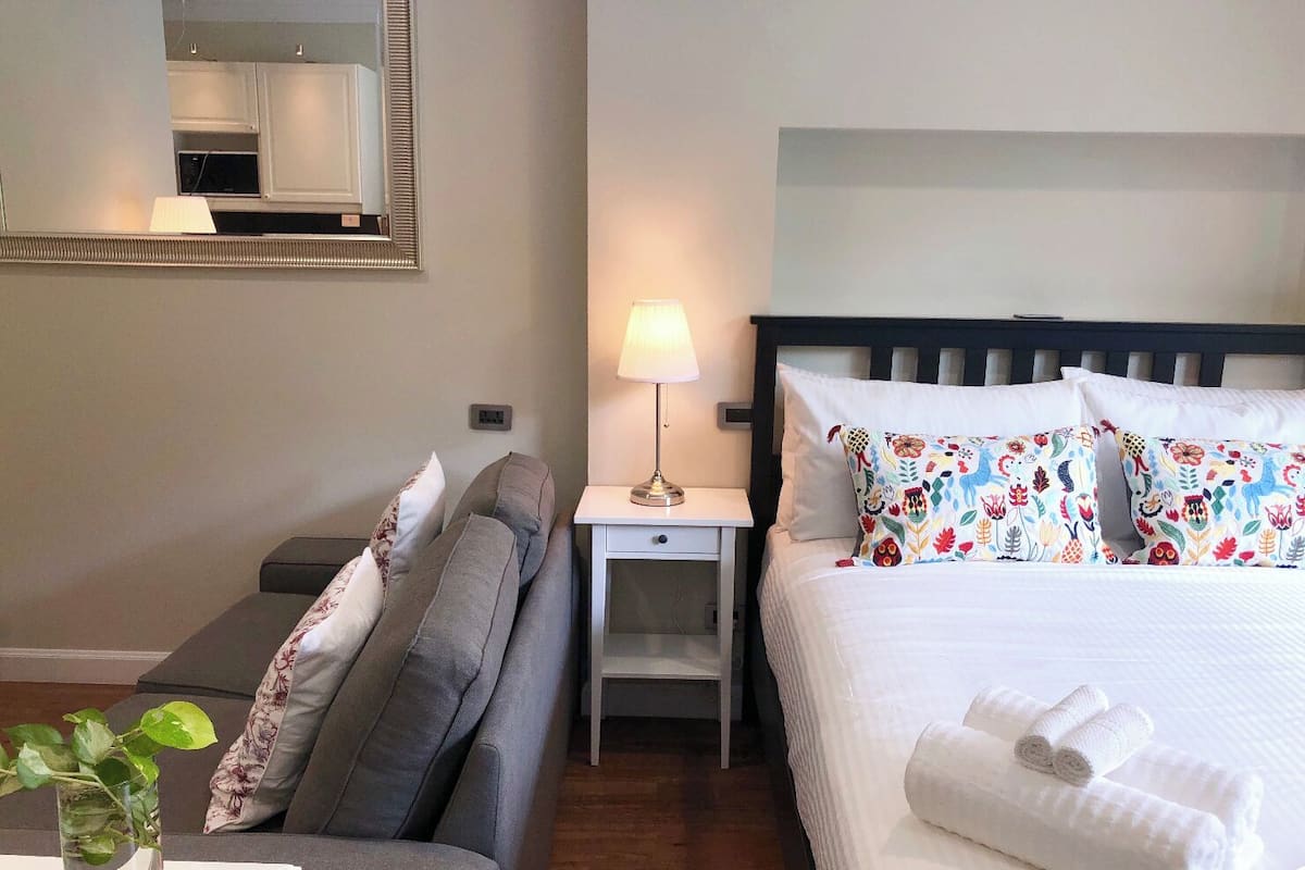 A hotel room with a bed, a sofa, a nightstand with a lamp, and a mirror on the wall.