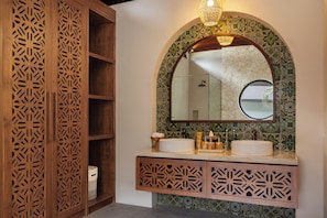 Un bagno con un armadietto in legno, uno specchio rotondo e un lavabo con zanzariera decorativa.