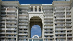 Een hotel met meerdere verdiepingen, balkons, een centrale boog en een heldere lucht.