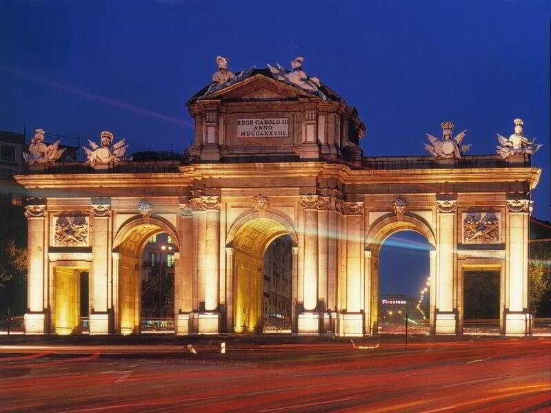 A grand, illuminated archway with classical sculptures and inscriptions, likely a historical monument.
