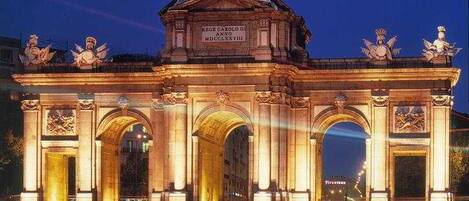 A grand, illuminated archway with classical sculptures and inscriptions, likely a historical monument.
