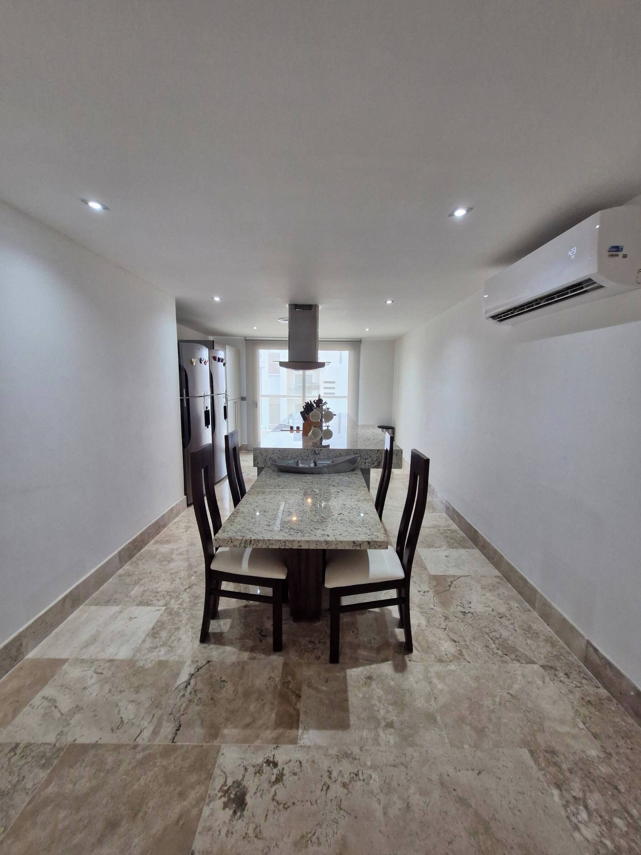 A modern kitchen with a central island, built-in appliances, and a large dining table with chairs.