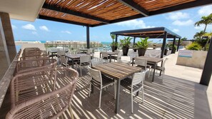 An outdoor patio with wicker furniture, metal tables, and chairs, overlooking a marina and the ocean. - Beautiful PH in Front of the Marina (Punta Sam)