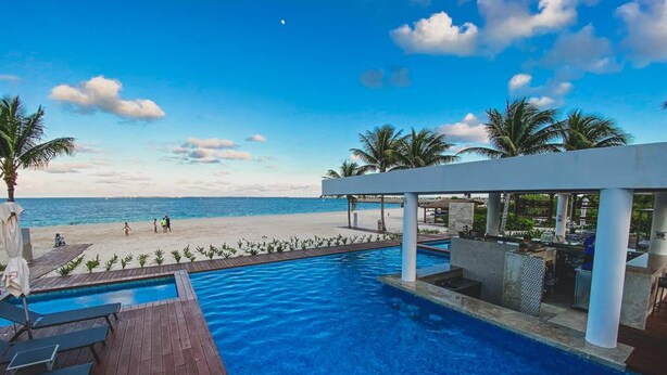 A pool with a view of the beach and ocean, surrounded by palm trees and a covered area with seating. - Beautiful PH in Front of the Marina (Punta Sam)