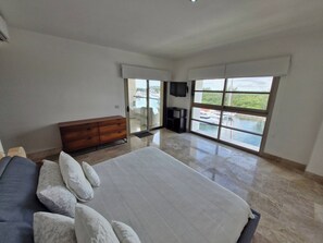 A bedroom with a large bed, a wooden dresser, a TV, and a balcony with a view of the water. - Beautiful PH in Front of the Marina (Punta Sam)