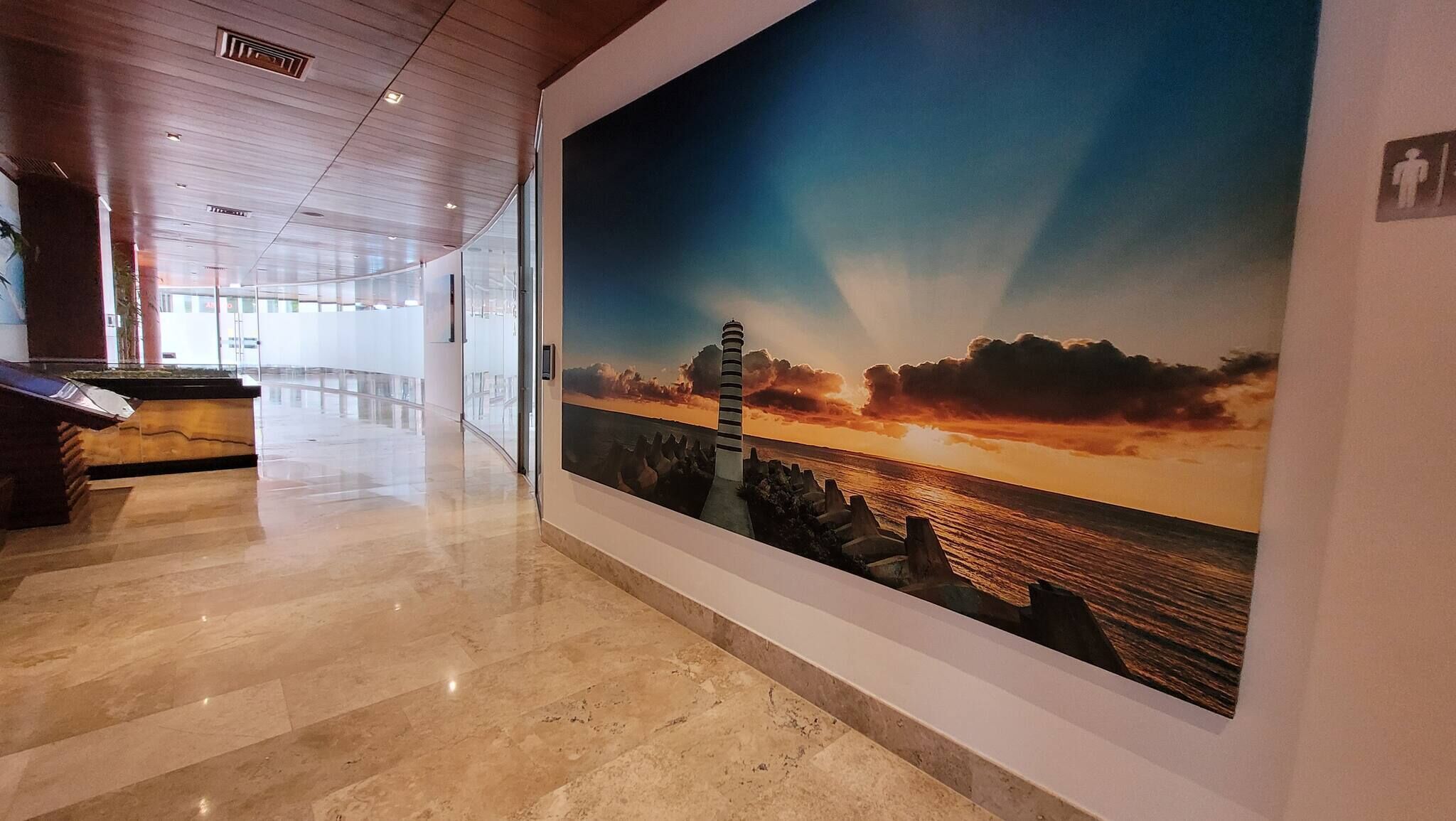 A corridor with a large mural of a lighthouse at sunset, a reception desk, and a glass wall.