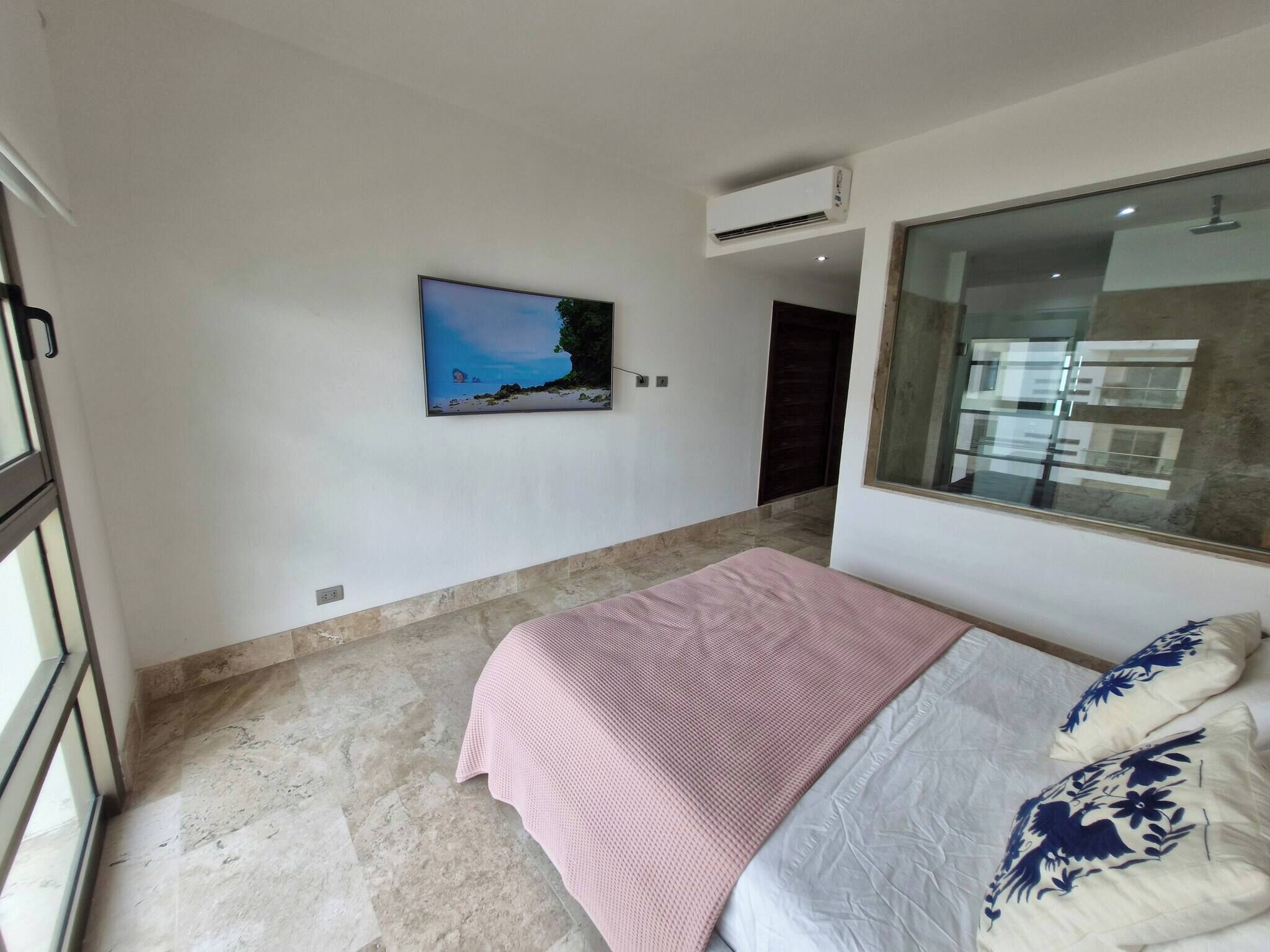 Un dormitorio con cama, televisor, aire acondicionado y ventana con vistas.
