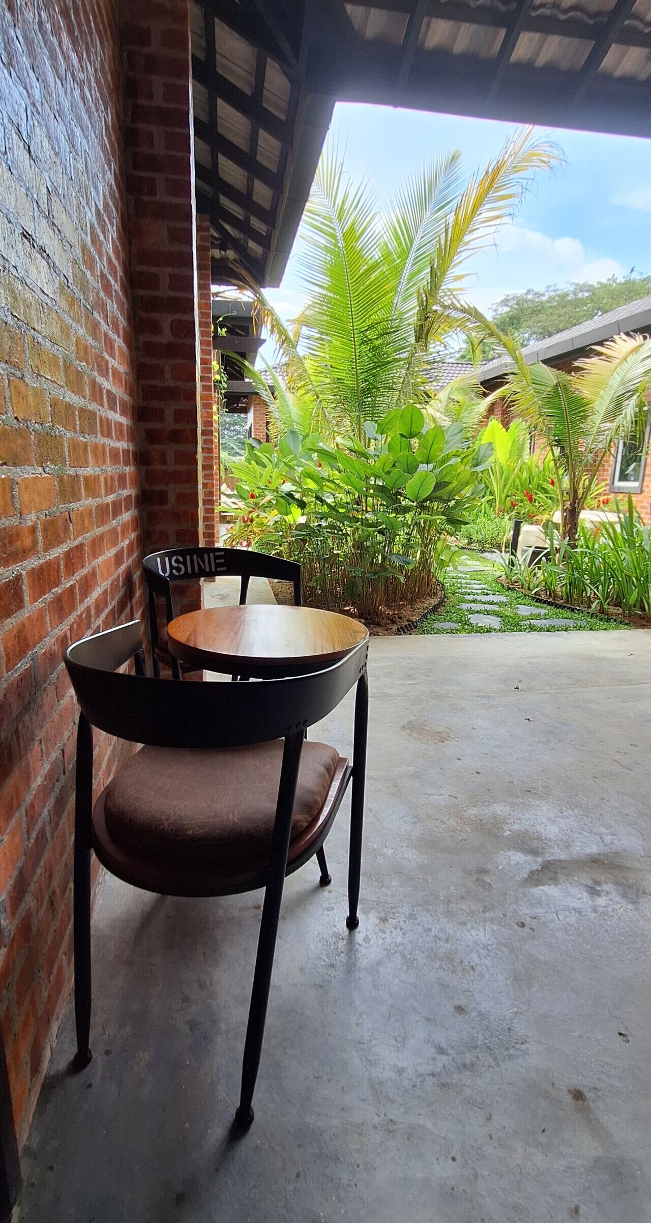 A brick wall, a table with a chair, and a garden with plants and a pathway.