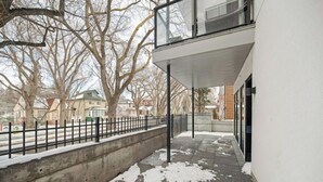 Un edificio moderno con base de concreto, balcón de vidrio y suelo cubierto de nieve.