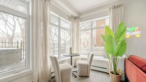 Una habitación con ventanas amplias, una mesa redonda, dos sillas, un sofá rojo y una planta verde.