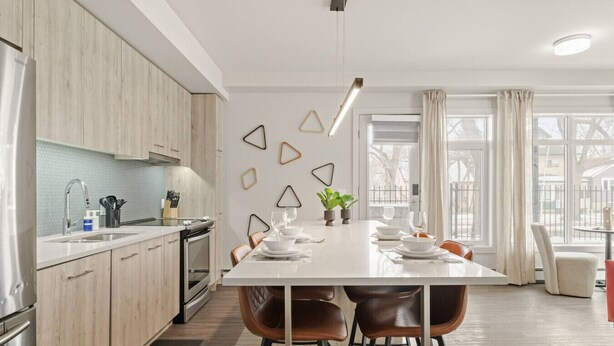 Una cocina moderna con comedor, armarios de madera, encimera blanca y una lámpara colgante.