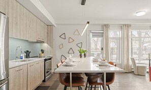 Een moderne keuken met een eethoek, houten kastjes, een wit aanrechtblad en een hanglamp.