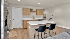 A modern kitchen with a central island, two bar stools, a refrigerator, and wooden cabinets. - Pearl Loft • Downtown CDA (Coeur d'Alene)