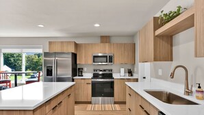 A modern kitchen with stainless steel appliances, wooden cabinets, and a large island with a sink. - Pearl Loft • Downtown CDA (Coeur d'Alene)