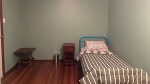 Une chambre à coucher avec un lit, une petite table en bois, une poubelle et un luminaire au plafond.