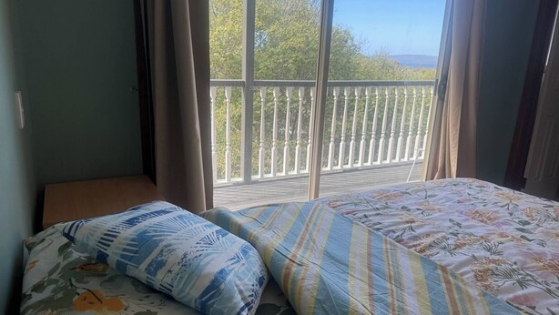 Une chambre à coucher avec un lit, une fenêtre avec des rideaux et un balcon doté d’une balustrade blanche.