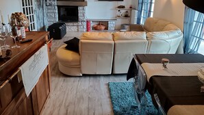 Ein Wohnzimmer mit Kamin aus Stein, einem Fernseher, einer Couch und einem Essbereich mit Tisch.