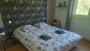 Ein Schlafzimmer mit einem Bett, einem Nachttisch, einer Lampe, einer Wand mit einem Blattmuster und einem Fenster.