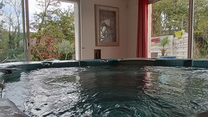 Ein Schwimmbecken mit klarem Wasser, umgeben von einer Ziegelmauer, und ein Fenster mit Blick auf Bäume und einen roten Vorhang.