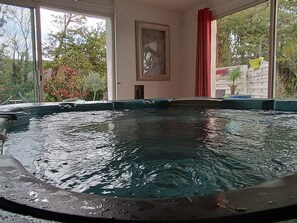 A swimming pool with clear water, surrounded by a brick wall, and a window with a view of trees and a red curtain. - Provencal house with swimming pool and spa. (Ris)