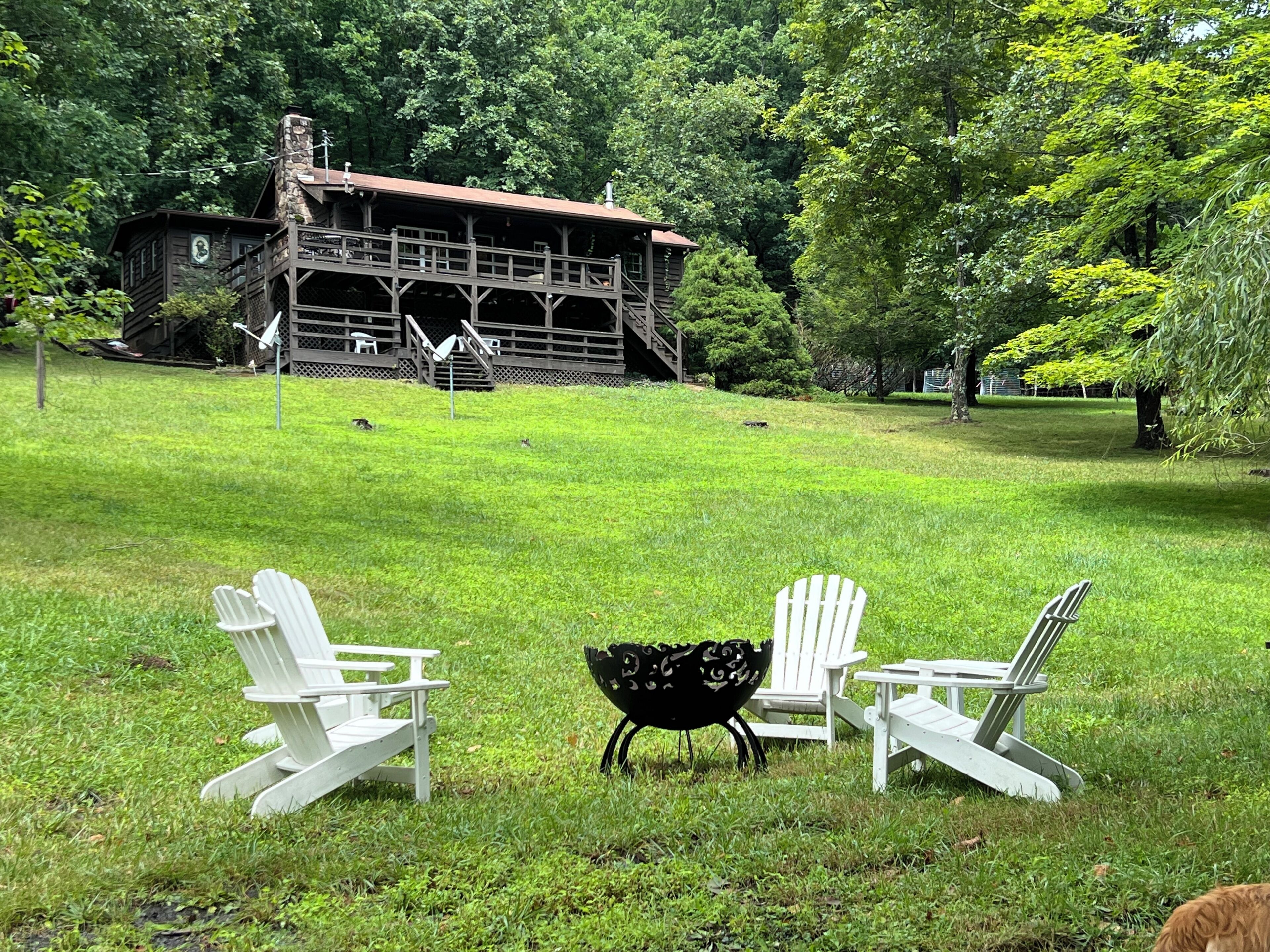 A grassy outdoor area with Adirondack chairs and a black metal table.