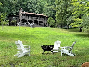 A grassy outdoor area with Adirondack chairs and a black metal table.