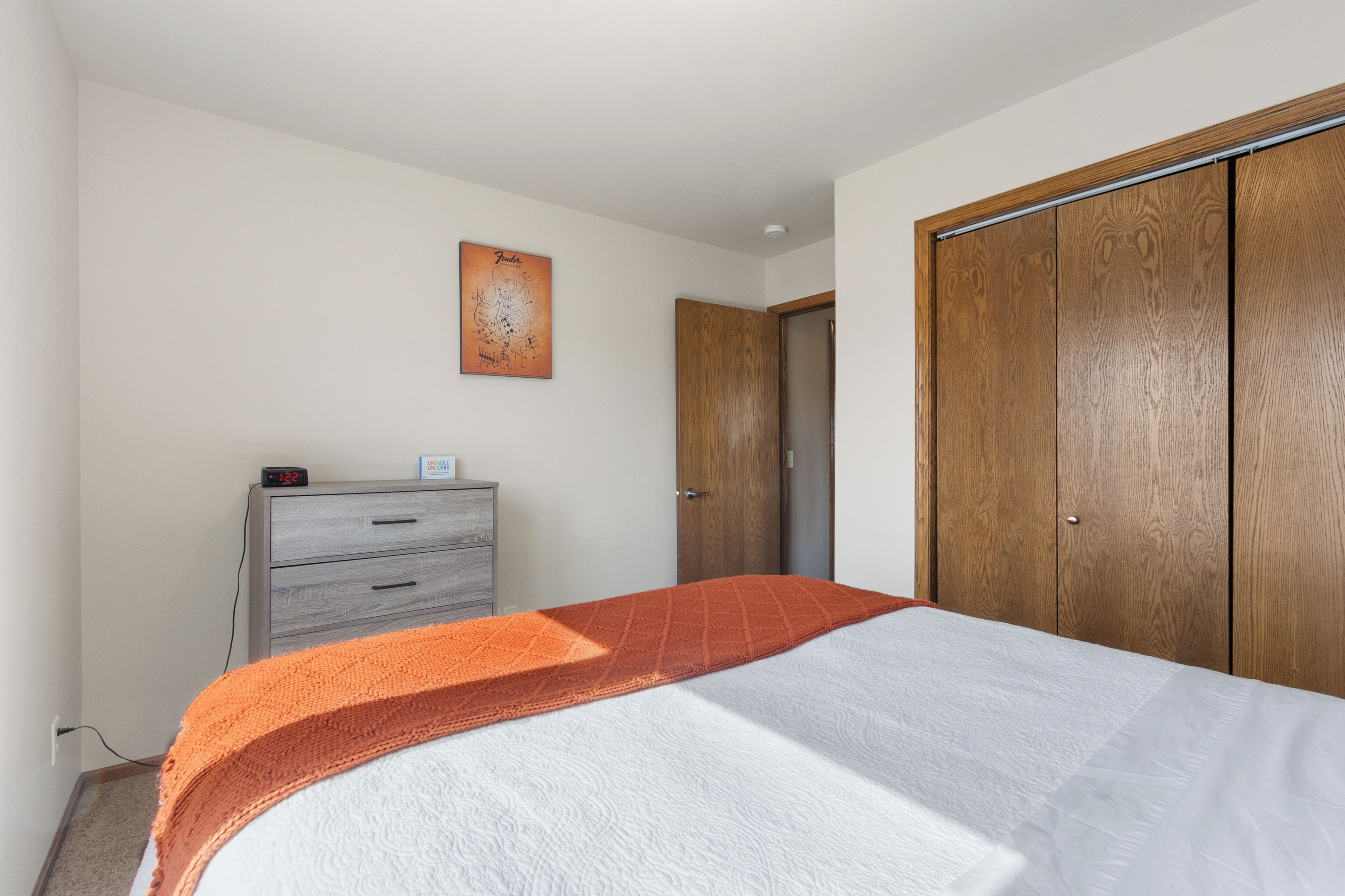 A bedroom with a bed, a dresser, a wooden wardrobe, and a wall clock.