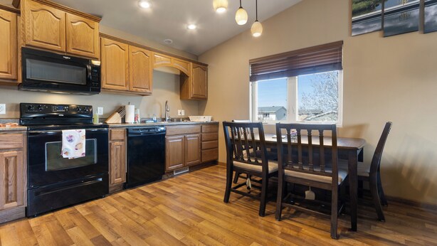 Una cocina con armarios de madera, un microondas negro y una zona de comedor con sillas y mesa de madera.