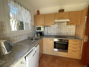 Eine kleine Küche mit Geschirrspüler, Backofen, Mikrowelle und einem fensterbepflanzten Fenster.