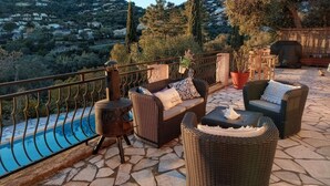 Una terraza en la azotea con mobiliario de mimbre, piscina y vistas a una colina.