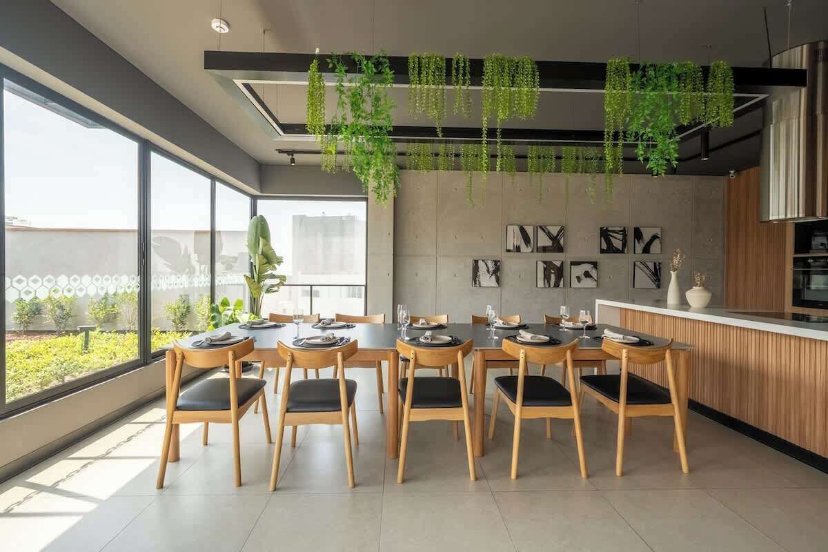 A dining area with a long table, chairs, hanging plants, and artwork on the wall.