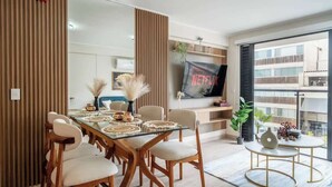 Un'area pranzo moderna con un tavolo in vetro, sedie in legno e un televisore montato a parete.