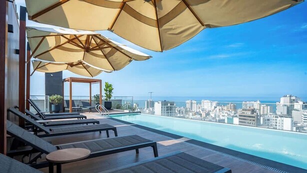 A rooftop infinity pool with lounge chairs and umbrellas, overlooking a cityscape. - Largest & Elegant Apartment | Larco | Miraflores (Miraflores)