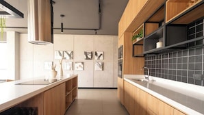 A modern kitchen with wooden cabinets, a white countertop, and black tiled backsplash. - Largest & Elegant Apartment | Larco | Miraflores (Miraflores)
