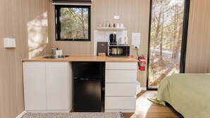 A compact kitchen with a sink, a coffee maker, and a microwave. There is a window with a view of trees and a fire extinguisher mounted on the wall.