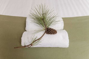 Una rama de pino con agujas y una piña sobre una toalla blanca doblada, sobre una superficie textil texturizada.