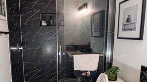 A modern bathroom with a glass-enclosed shower, a toilet, and a sink. - The Loft Moden Rental (Calgary)