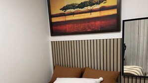 A bedroom with a bed, a painting, a window with curtains, and a striped wall panel. - The Loft Moden Rental (Calgary)