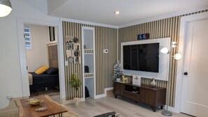 A modern living room with a TV, wooden furniture, and striped wallpaper. - The Loft Moden Rental (Calgary)