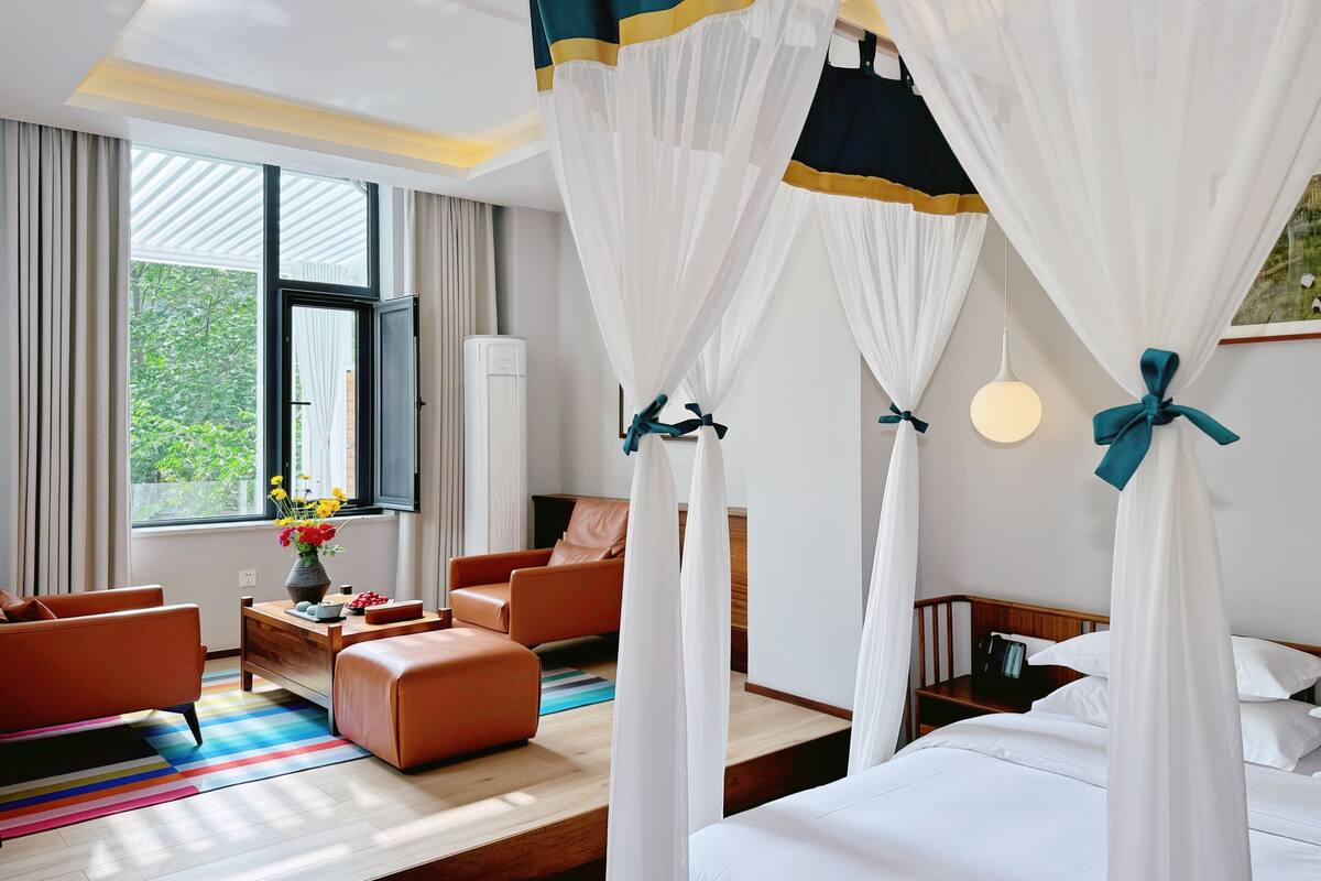 A hotel room with a bed, two armchairs, a coffee table, and a window with curtains.