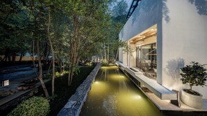 Een modern gebouw met een waterpartij, omringd door bomen en een stenen pad.