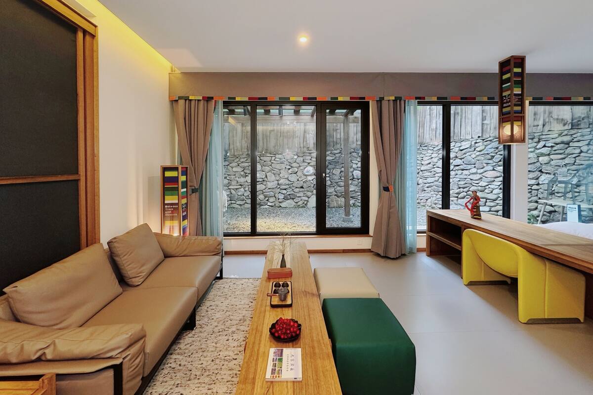 A modern living room with a sofa, a dining table, and a view of a stone wall outside.