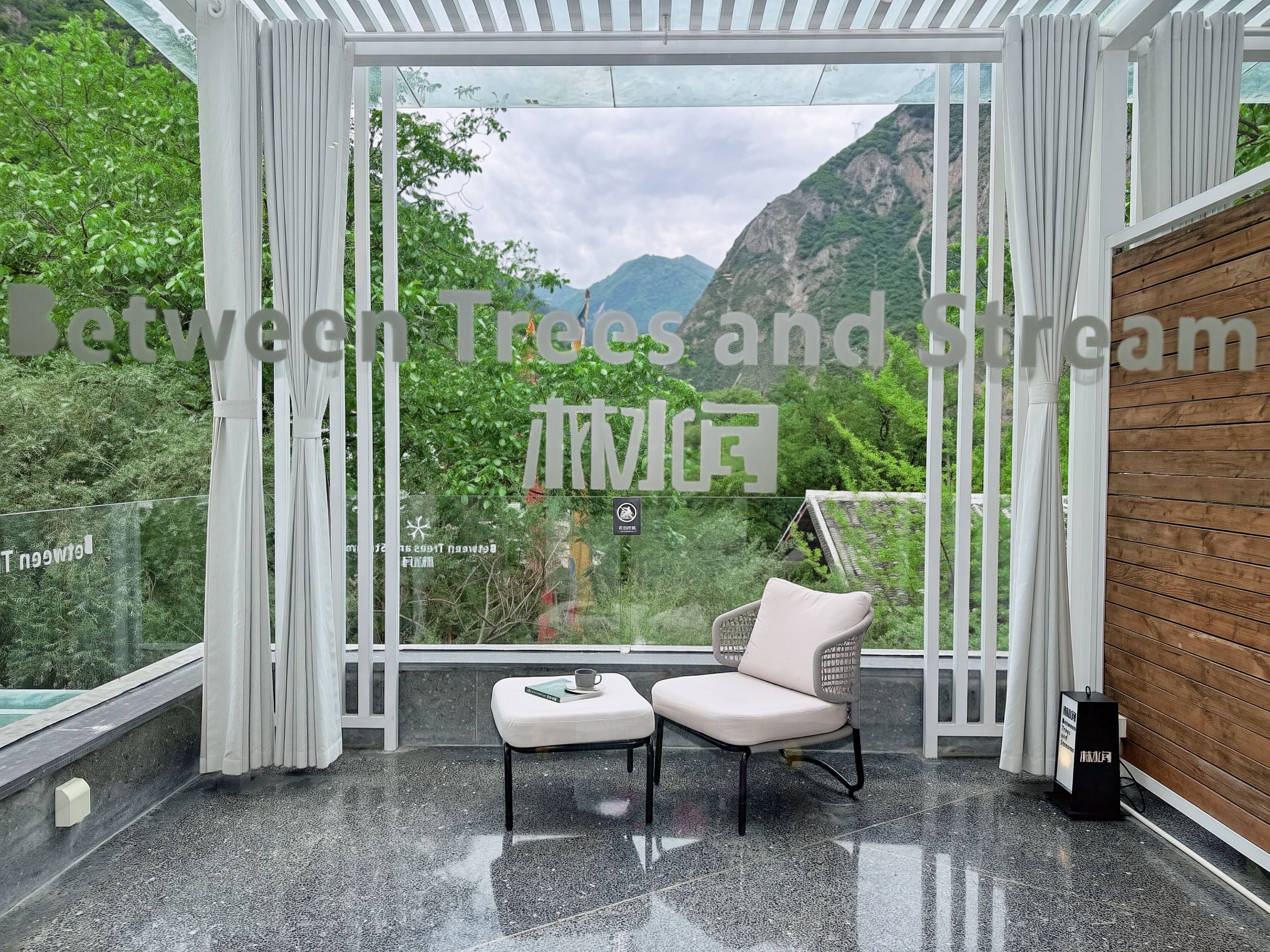 A room with a large window, a white chair, a small table, and a wooden wall.